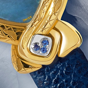 Fang Yin, Subtile montre en or délicatement gravée et son cadran de nacre bleu ornée d'un bluet. Le cabochon en acier est serti de 3 saphirs. Le bracelet de cuir bleu l'achève en beauté.
